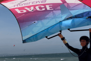 Liz Kaiser wing foiling on Mui Ne Beach, wearing a life jacket and helmet, with a focused smile, as she embraces a new challenge in her journey in Mui Ne.